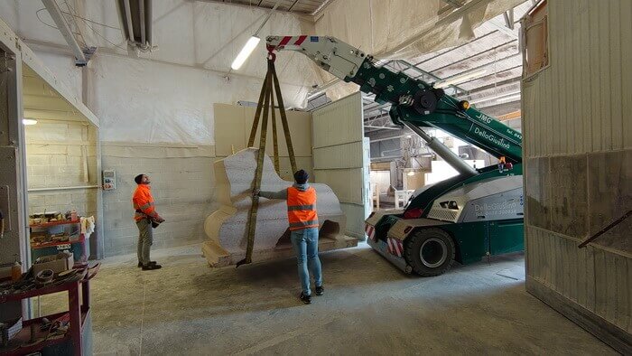 A skilled worker expertly moves the red marble block with a radio-controlled self-propelled crane